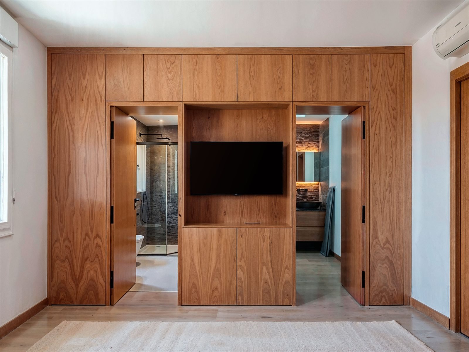 Armario de madera con las puertas ocultas abiertas revelando el acceso a los dos baños