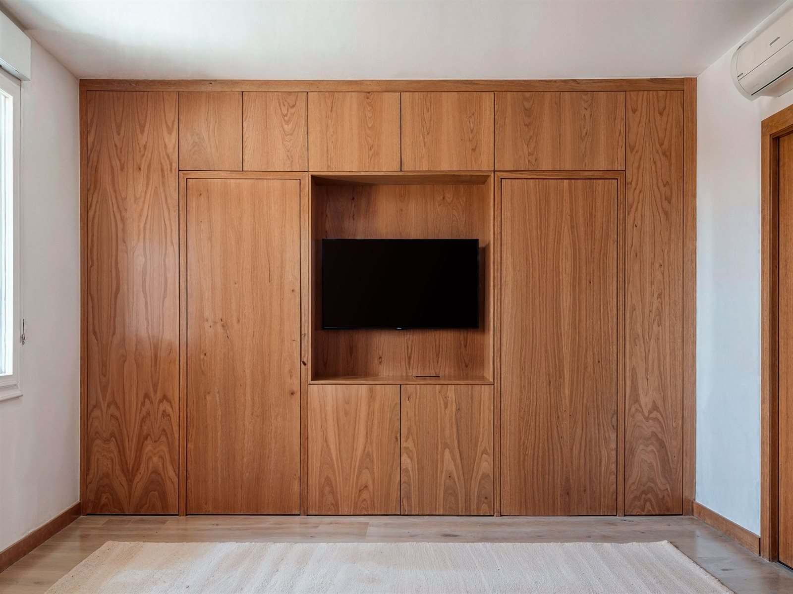 Armario de madera con puertas ocultas cerrado: panelado continuo con hueco para la televisión