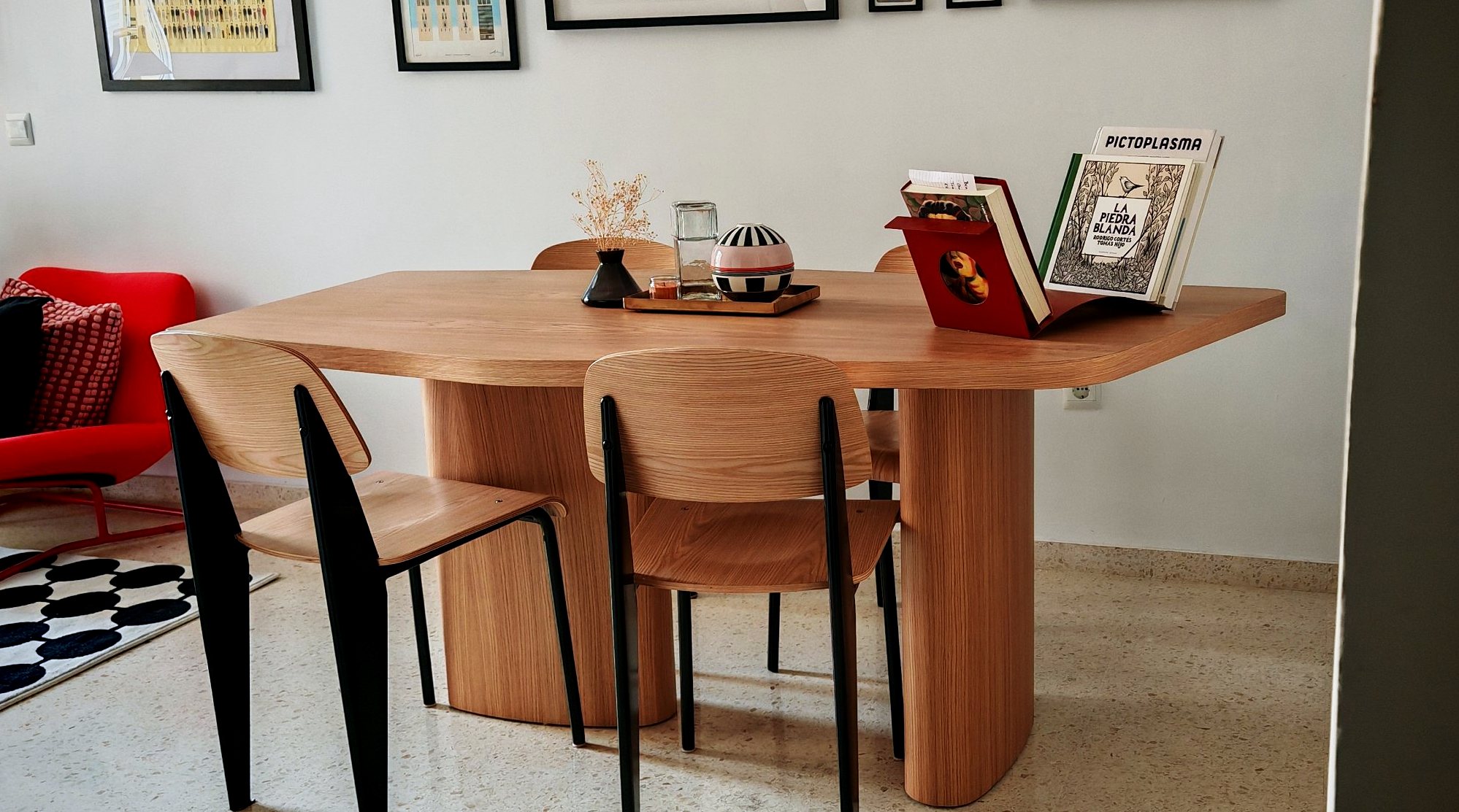 Mesa de forma libre de roble con sillas Prouvé junto a una butaca roja