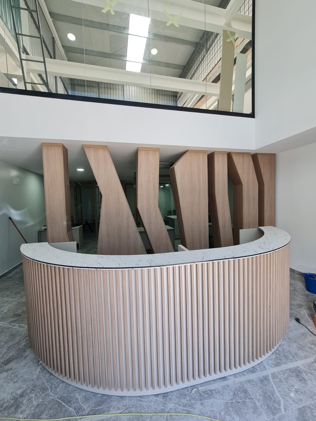 Mostrador de recepción curvo a medida con frente de listones de madera, foto de obra